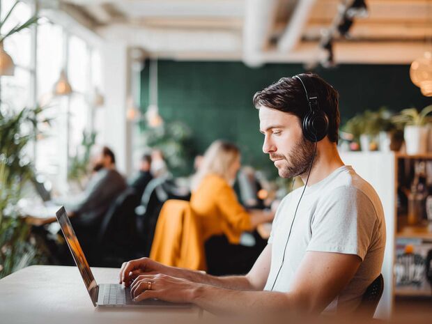 Mann mit Kopfhörern arbeitet konzentriert am Laptop in einem Coworking-Space