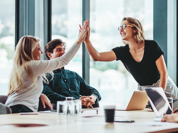 Un uomo e due donne siedono felicemente a un tavolo. I computer portatili sono davanti a loro e le due donne si danno il cinque.