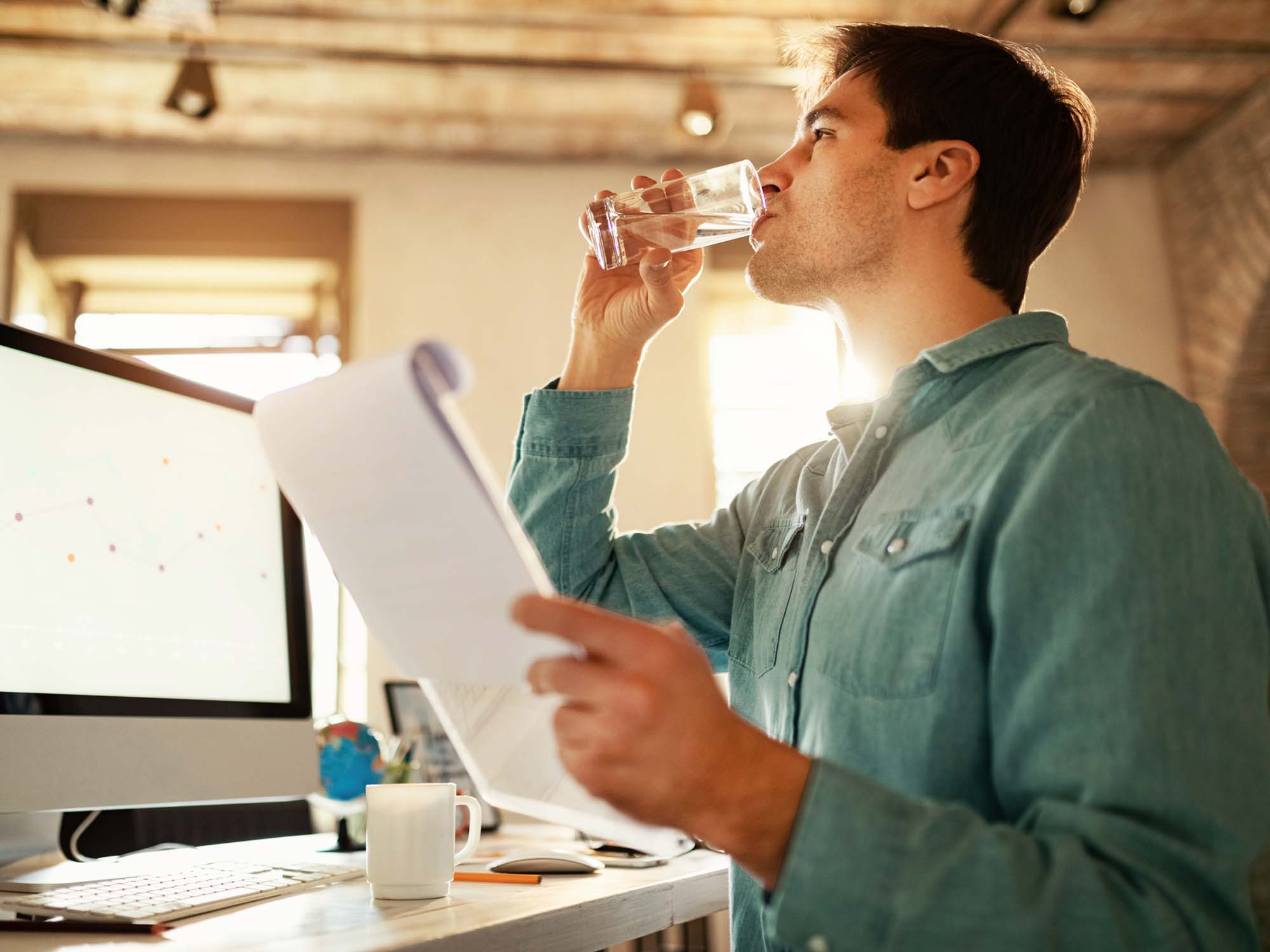 At his desk, he drinks a glass of water and holds a clipboard in his hand