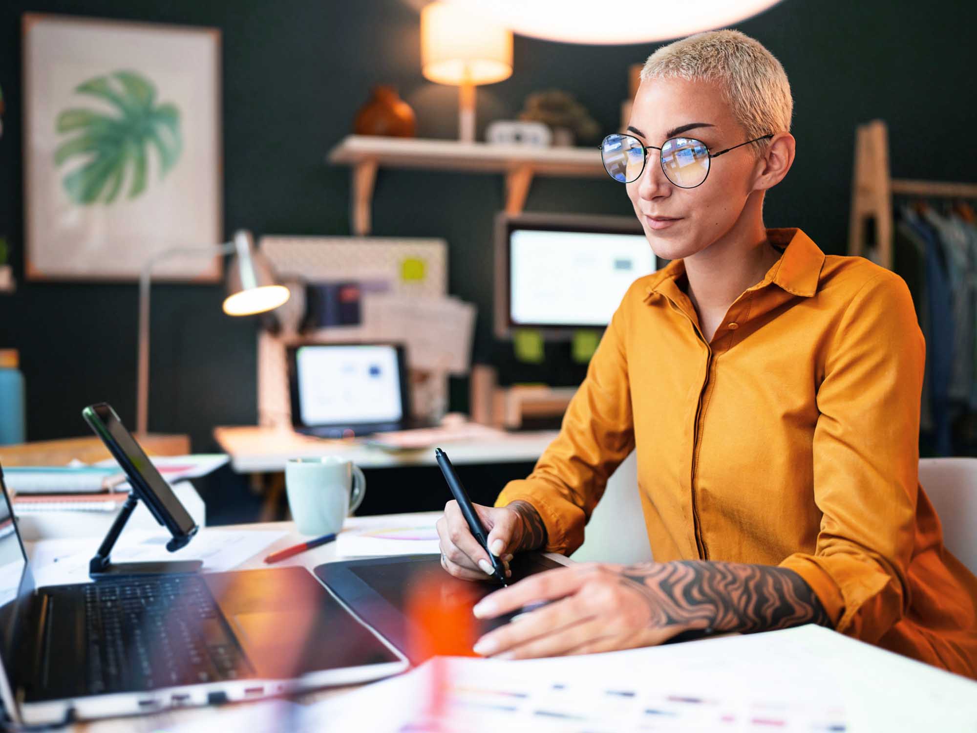 Woman with glasses at a desk, drawing on a graphics tablet