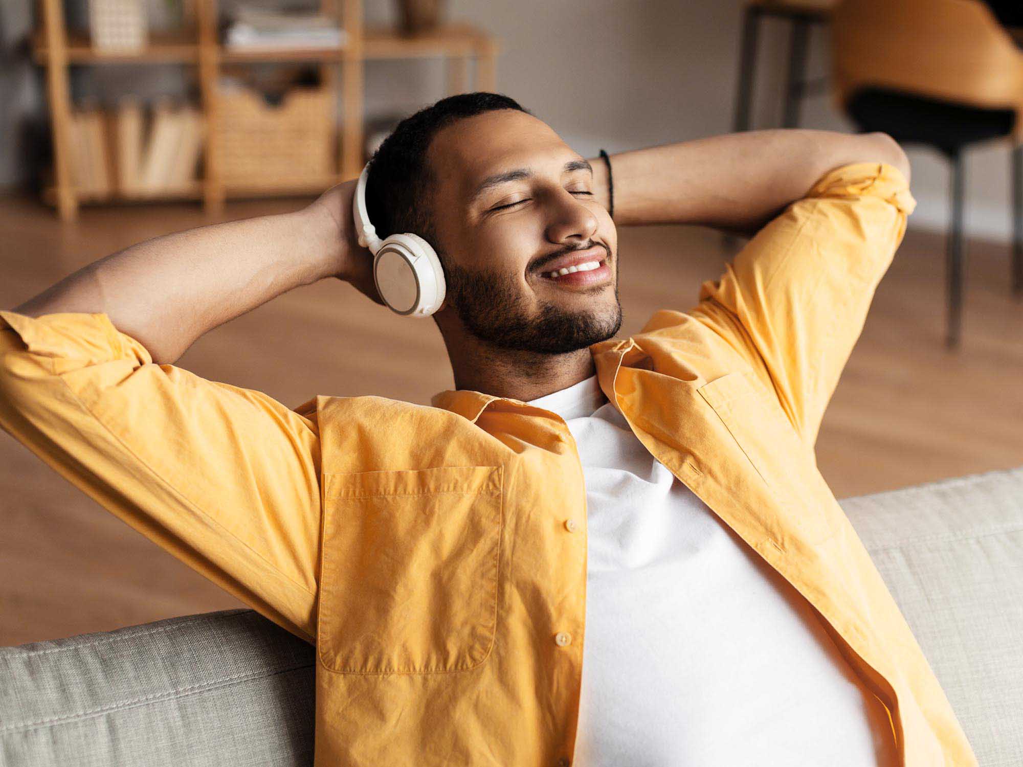 Man sitting on the couch, smiling, leaning back and wearing headphones